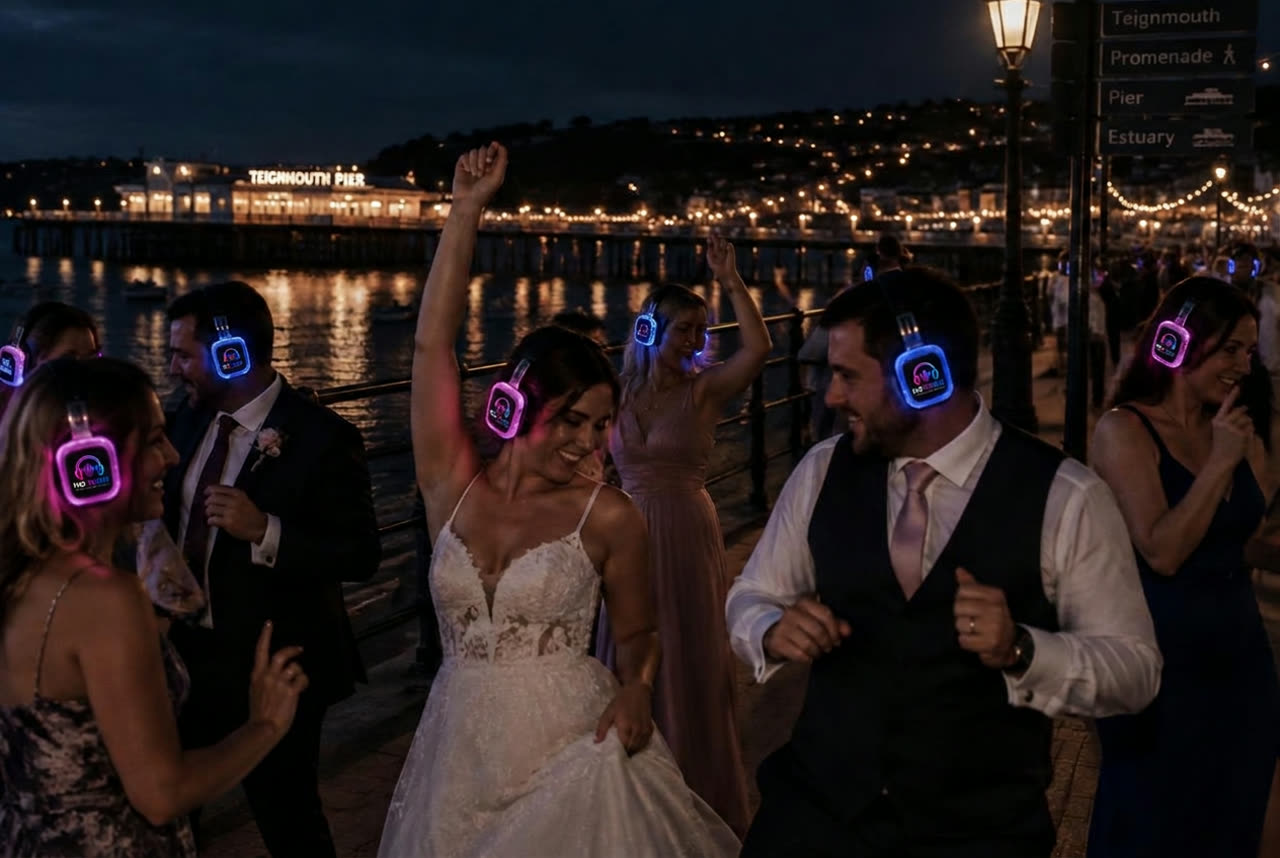 Wedding guests dancing in No Noise silent disco headphones on Teignmouth seafront with the pier lit behind